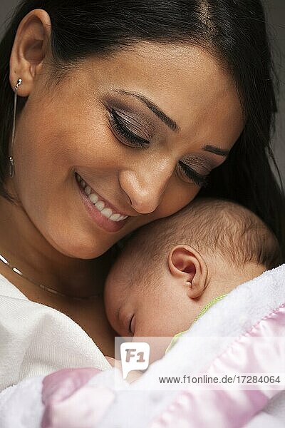Young attractive ethnic woman holding her newborn baby under dramatic lighting