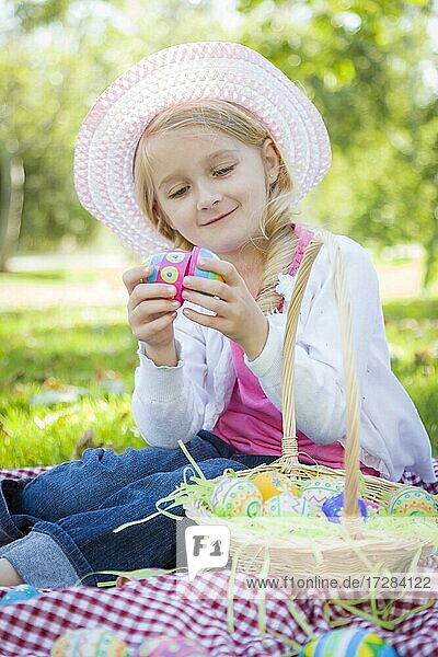 Nettes junges Mädchen auf Picknick-Decke trägt Hut genießt ihre Ostereier draußen im Park