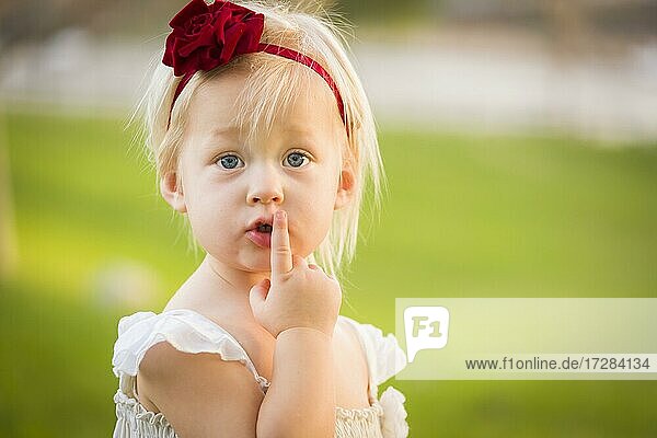 Schöne bezaubernde kleine Mädchen mit ihrem Finger auf den Mund tragen weißes Kleid in einem Grasfeld