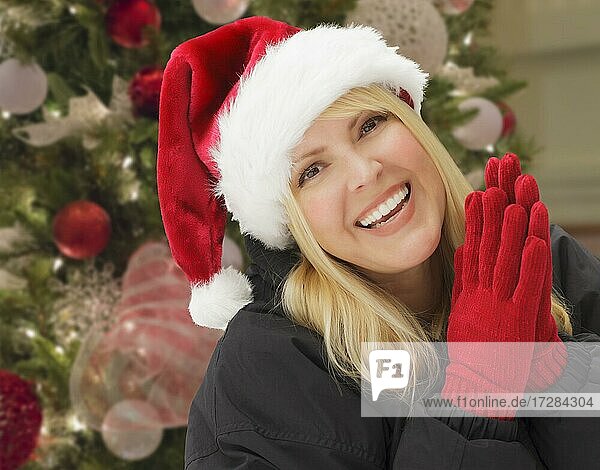 Beautiful woman wearing santa hat and mittens in front of christmas tree