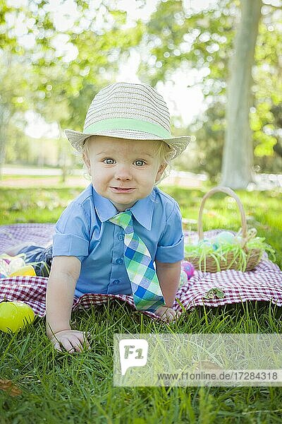 Netter kleiner Junge lächelt auf Picknickdecke mit Ostereiern um ihn herum