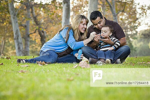 Happy young mixed-race ethnic family playing together with bubbles in the park