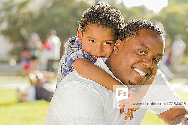 Glücklicher afrikanischer amerikanischer Vater und gemischtrassiger Sohn spielen Huckepack im Park