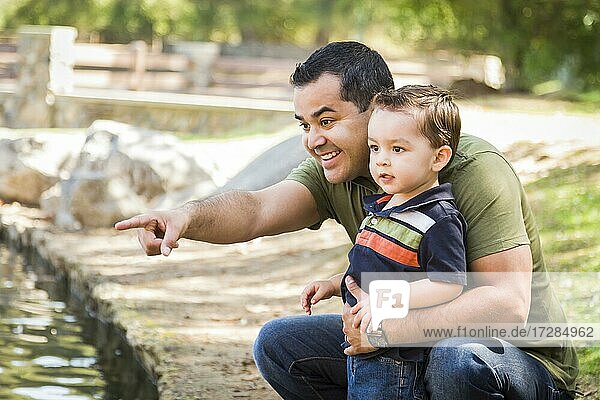 Glücklicher hispanischer Vater zeigt mit gemischtrassigem Sohn am Parkteich