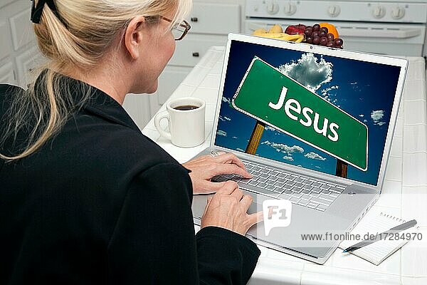 Frau in der Küche mit Laptop mit Jesus-Straßenschild auf dem Bildschirm. Bildschirm kann leicht für Ihre eigene Nachricht oder Bild verwendet werden