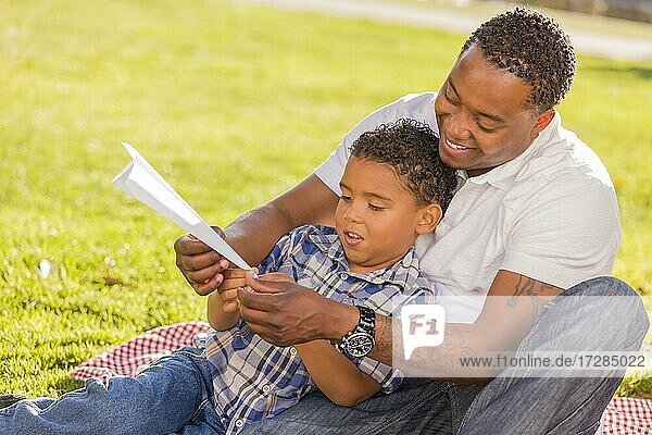 Glücklicher afrikanischer amerikanischer Vater und gemischtrassiger Sohn spielen mit Papierfliegern im Park