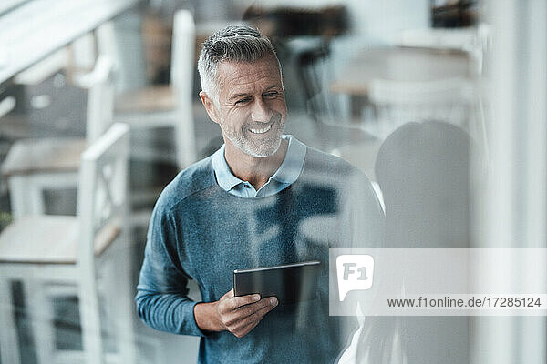 Lächelnder männlicher Unternehmer mit digitalem Tablet  der einen Kollegen in einem Café anschaut