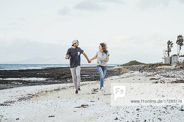 Unbekümmertes Paar  das sich beim Laufen am Strand an den Händen hält