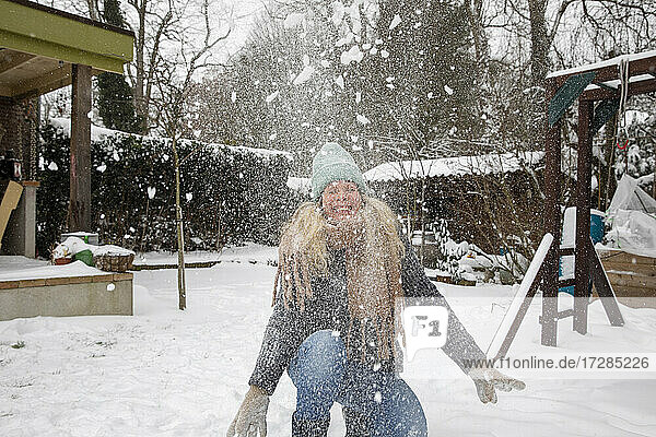 Glückliche reife Frau spielt mit Schnee im Hinterhof