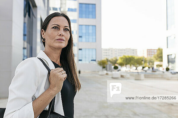 Geschäftsfrau mit Handtasche schaut weg  während sie auf dem Fußweg wartet