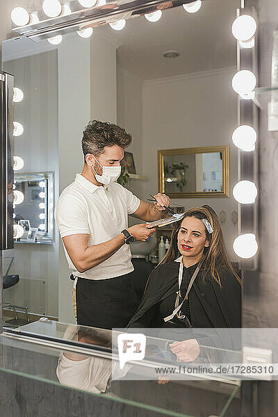 Spiegelreflexion eines männlichen Experten  der einer Kundin im Salon die Haare färbt