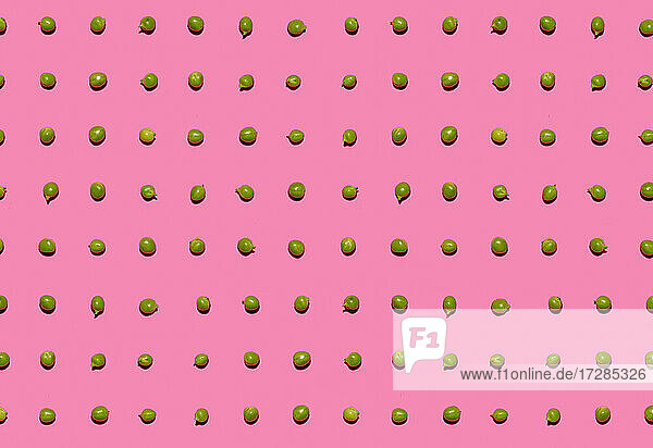 Pattern of green peas flat laid against pink background