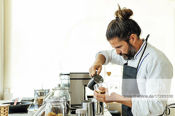 Professioneller Koch gießt Milch ein  während er Kaffee in einem modernen Restaurant zubereitet
