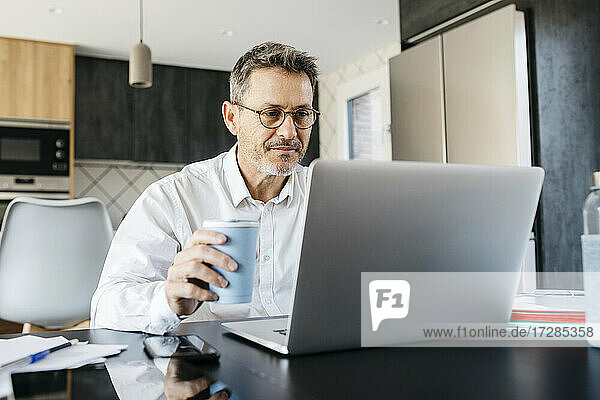 Geschäftsmann trinkt Kaffee  während er im Büro zu Hause am Laptop arbeitet