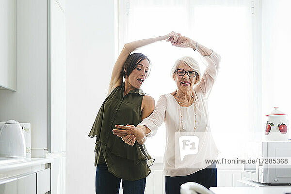 Mittlere erwachsene Frau mit Großmutter  die in der Küche zu Hause tanzen und sich an den Händen halten