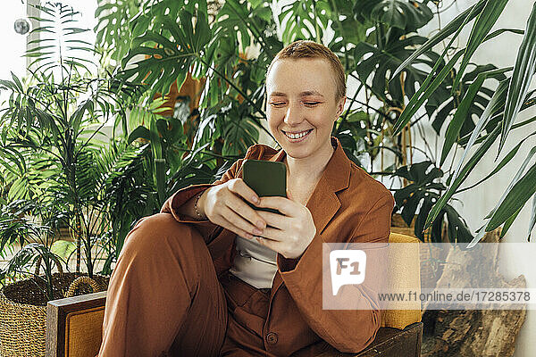 Lächelnde junge Geschäftsfrau  die ein Smartphone in einem grünen Büro benutzt