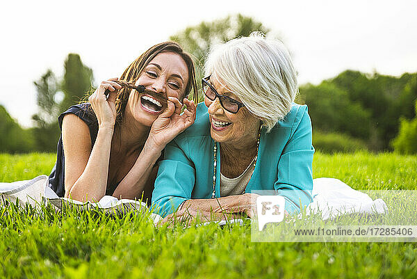 Fröhliche Enkelin spielt mit den Haaren  während sie neben der Großmutter auf der Wiese liegt