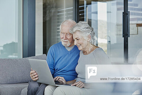 Smiling senior couple using laptop sitting in living room at home
