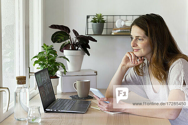 Lächelnde weibliche Fachkraft bei einem Videogespräch am Laptop im Büro zu Hause
