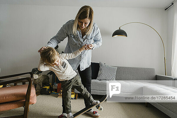 Blonde Frau hilft ihrem Sohn  zu Hause Skateboard fahren zu lernen