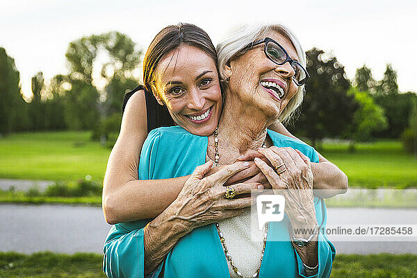 Lächelnde Enkelin umarmt Großmutter von hinten im Park