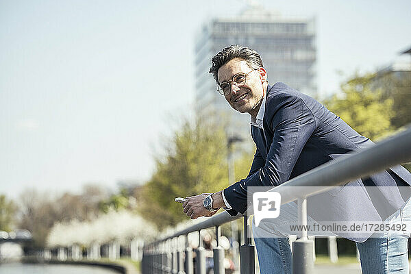Smiling male entrepreneur leaning on railing during sunny day