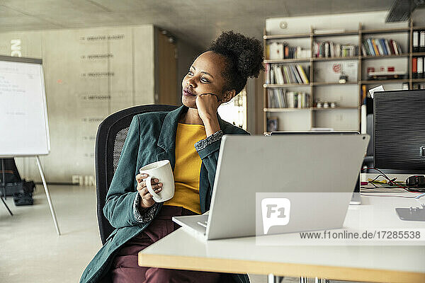 Geschäftsfrau mit Kaffeebecher  die am Schreibtisch sitzt und nachdenkt