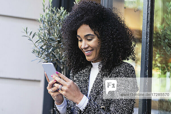 Lächelnde Frau mit Smartphone in der Nähe des Fensters vor einer Bar