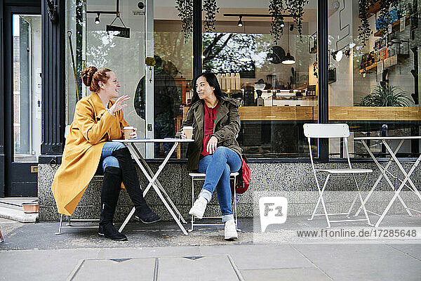 Frau gestikuliert im Gespräch mit einer Freundin vor einem Café