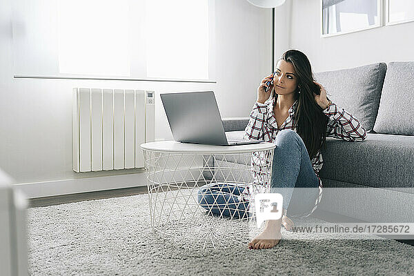 Woman talking on mobile phone while sitting on carpet at home
