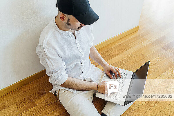 Junger Mann benutzt Laptop  während er zu Hause auf dem Boden sitzt