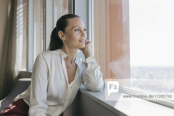 Schöne Unternehmerin schaut durch das Fenster  während sie im Büro sitzt