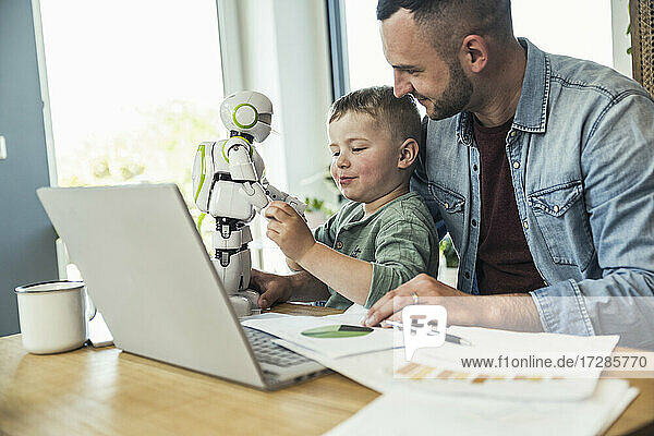 Smiling man looking at son playing with robot at home