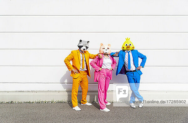 Drei Personen in farbenfrohen Anzügen und Tiermasken posieren nebeneinander vor einer weißen Wand