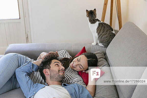 Lächelndes Paar mit getigerter Katze auf dem Sofa im Wohnzimmer liegend im Zimmer