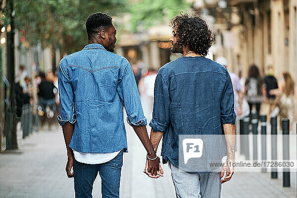 Homosexuelles Paar  das sich an den Händen hält und sich gegenseitig anschaut  während es auf dem Fußweg geht