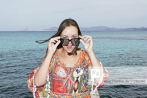 Ältere Frau mit Sonnenbrille und offenem Mund steht vor dem Wasser auf der Insel Formentera