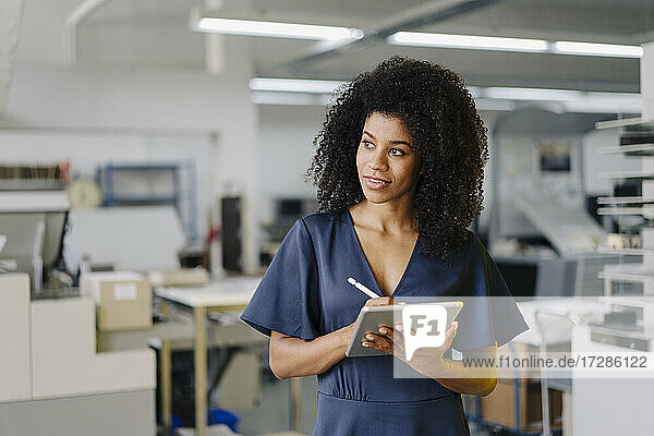 Afro-Frau schaut weg  während sie ein digitales Tablet im Büro hält