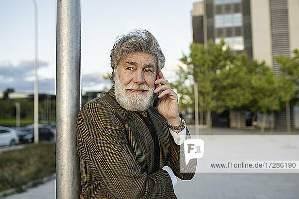 Älterer Geschäftsmann lehnt sich an einen Pfahl  während er mit seinem Handy in der Stadt telefoniert