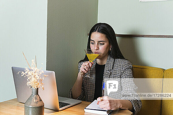Geschäftsfrau trinkt etwas  während sie im Restaurant am Laptop arbeitet