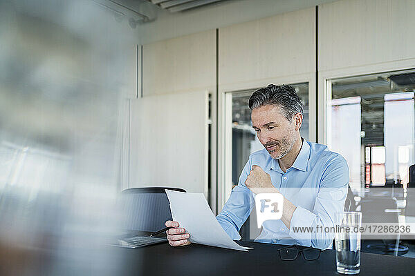 Male professional reading documents while sitting at desk in office