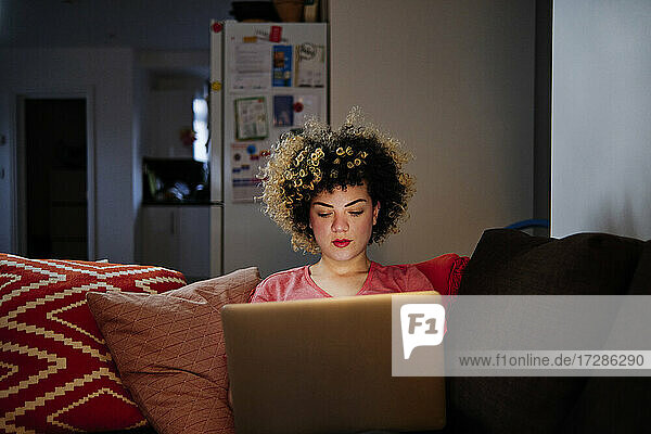 Schöne junge Frau mit Laptop sitzt auf dem Sofa im Wohnzimmer zu Hause