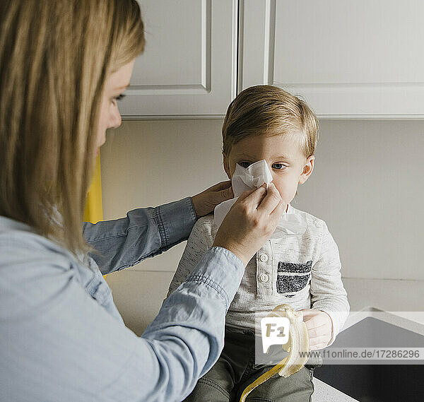 Mother cleaning son's nose at home