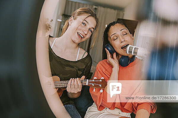 Mädchen spielt Ukulele  während Frau zu Hause am Mikrofon singt