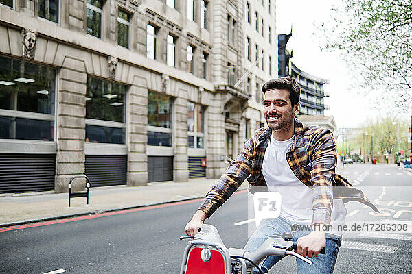 Smiling man wearing plaid shirt cycling on road in city