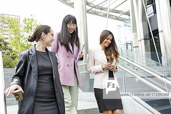Lächelnde Geschäftsfrauen mit Einweg-Kaffeebecher auf der Treppe