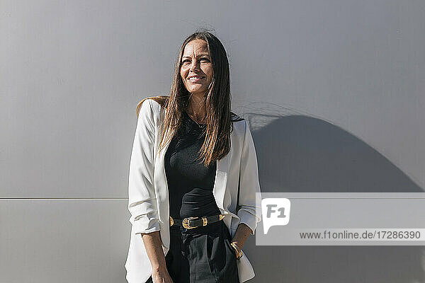 Smiling mature businesswoman standing in front of gray wall