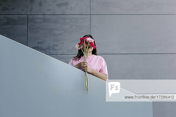 Frau hält einen Strauß Gerbera-Gänseblümchen vor dem Gesicht am Geländer
