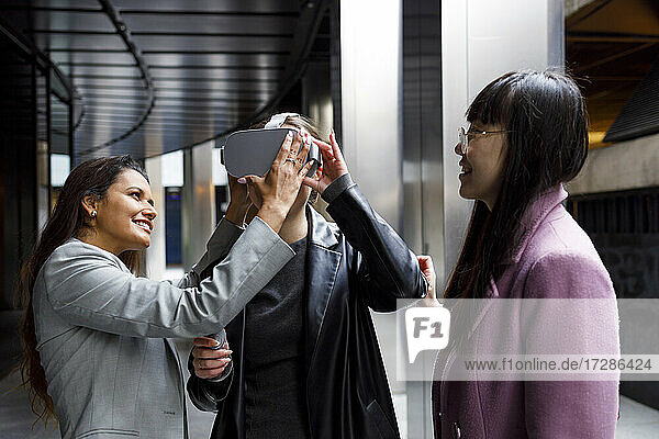 Eine Geschäftsfrau hilft einem Kollegen beim Einstellen eines Virtual-Reality-Headsets im Korridor