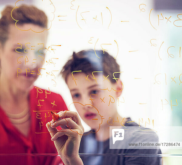 Junge schreibt mit seiner Mutter auf Glas  während er zu Hause Mathematik lernt